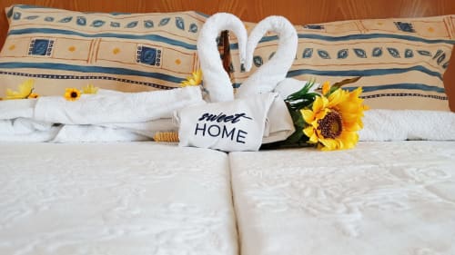 Quarto acolhedor do Sweet Home Paraiso Sol da Rocha em Portimão com cisnes de toalha, girassóis e placa de bem-vindo sobre fundo branco