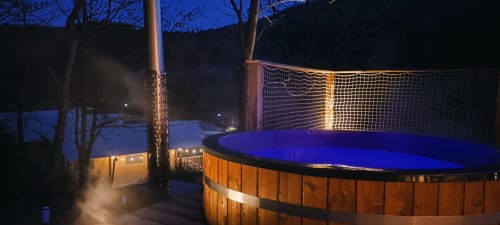 Illuminated wood-fired hot tub at night with blue water, overlooking mountains at Les Cabanes du Nideck in Oberhaslach