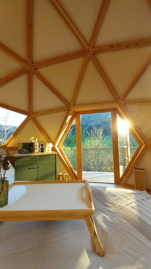 Geodesic dome interior at Les Cabanes du Nideck with wooden frame, bed, green dresser, and mountain views from balcony doors