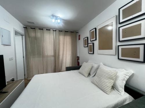 Dormitorio moderno en ML Apartments Valencia con cama blanca, almohadas grises, cuadros decorativos, cortinas beige y luminaria de techo