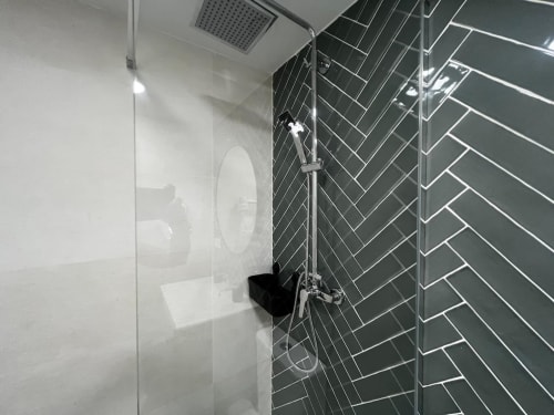 Elegante baño moderno con pared de ducha en azulejos tipo espiga gris oscuro y mampara de cristal en ML Apartments, Valencia