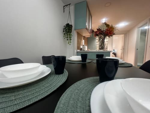 Comedor moderno en ML Apartments Valencia con mesa negra, vajilla blanca, individuales verdes, plantas colgantes y