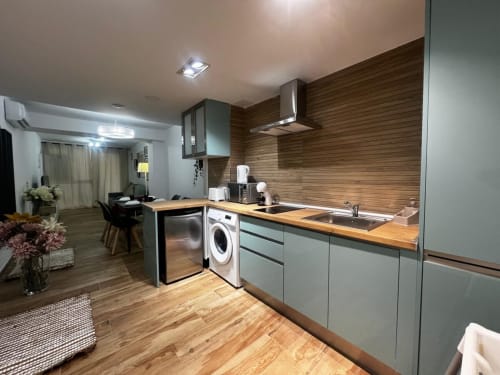 Cocina moderna en ML Apartments Valencia con armarios verde salvia, encimeras de madera, electrodomésticos de acero inoxidable y