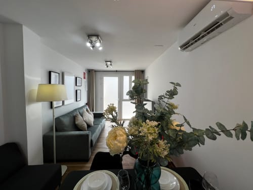 Moderno apartamento en Valencia con comedor, flores amarillas, sofá negro y aire acondicionado junto a Playa Malvarrosa