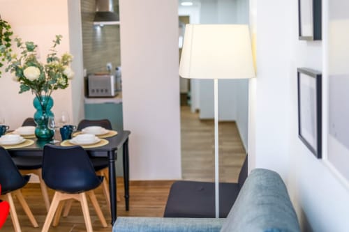 Área de comedor moderna en ML Apartments Valencia con mesa negra, sillas azules, florero turquesa y lámpara de pie