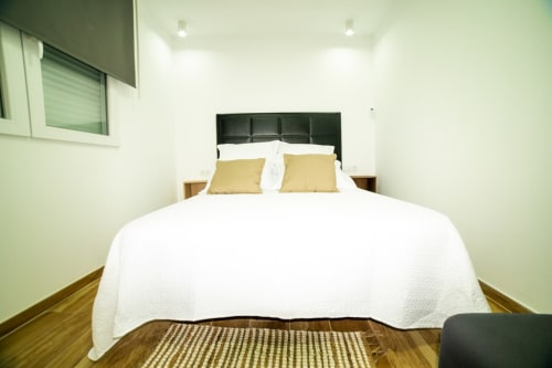 Dormitorio luminoso en ML Apartments Valencia con ropa de cama blanca, almohadas amarillas, cabecero negro, piso de madera y ventana con