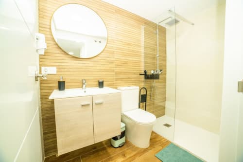 Baño moderno en ML Apartments Valencia con revestimiento de madera, espejo redondo, lavabo doble y ducha walk-in