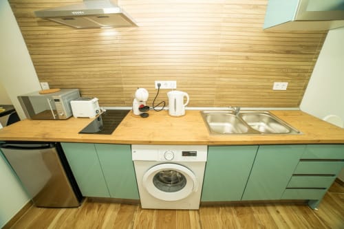 Cocina moderna en apartamento de Valencia con muebles verde menta, encimera de madera, lavadora, fregadero y electrodomésticos
