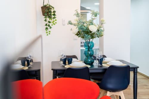 Comedor moderno con mesa negra, sillas rojas, jarrón azul con flores, plantas colgantes, apartamento en Valencia