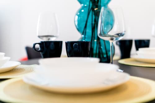 Elegante mesa de comedor en ML Apartments Valencia con individuales dorados, platos blancos, tazas negras y cristalería turquesa