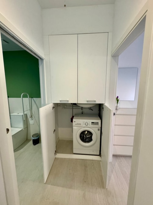 Lavadora integrada en pequeño cuarto de lavandería en ML Apartments Valencia, con muebles blancos y pisos de madera
