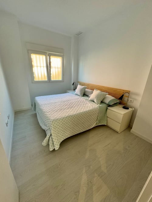 Dormitorio moderno en ML Apartments Valencia con cama doble, cabecero de madera, mesita blanca y ventana con luz natural