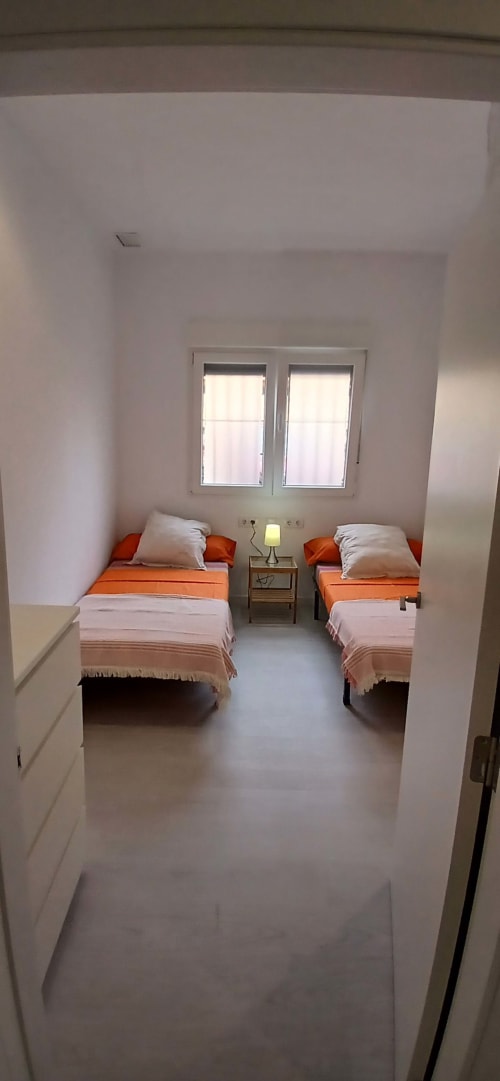 Habitación doble con ropa de cama naranja en ML Apartments Valencia, camas gemelas con almohadas blancas, mesita de noche con lámpara y ventana