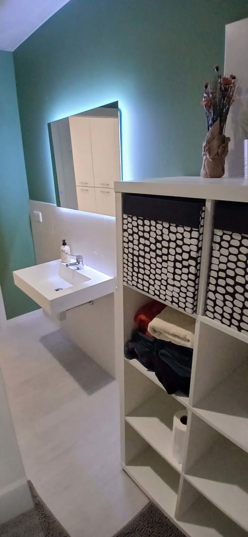 Baño moderno en ML Apartments Valencia con lavabo blanco, paredes verdes, espejo iluminado y estantería blanca de almacenamiento con