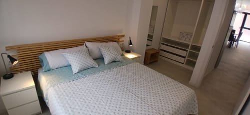 Dormitorio moderno en ML Apartments Valencia con cabecero de madera, ropa de cama blanca y armario empotrado