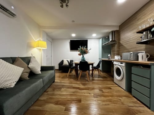 Sala de estar moderna con sofá gris, mesa de comedor, cocineta con electrodomésticos y pisos de madera en ML Apartments