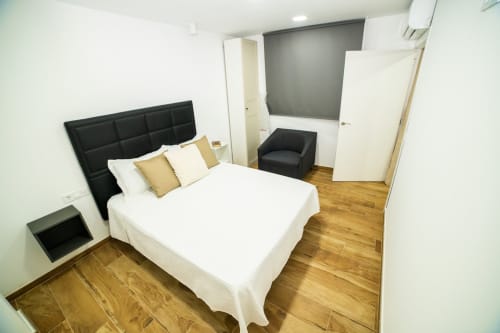 Dormitorio moderno en ML Apartments Valencia con cama queen, cabecera negra, suelos de madera y pared gris