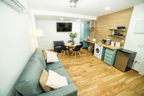 Apartamento moderno de planta abierta en ML Apartments Valencia con sofá gris, mesa de comedor de madera, cocina con electrodomésticos y