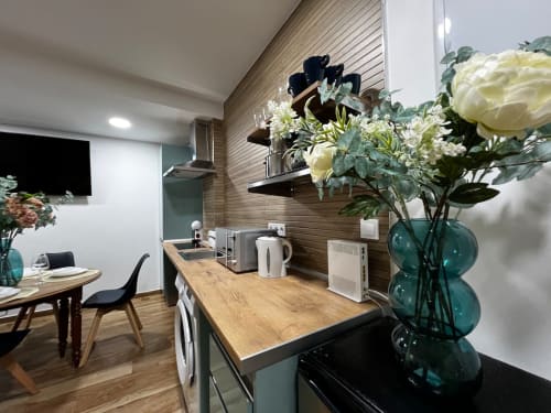 Cocina moderna con encimera de madera, jarrón turquesa con flores blancas y zona de comedor en ML Apartments Valencia