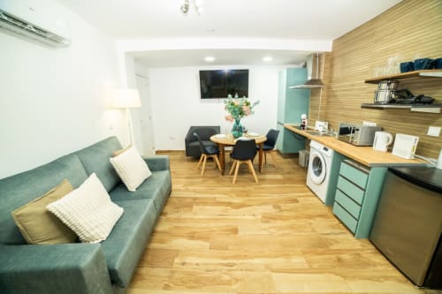 Moderno apartamento en Valencia con sofá verde, cocina americana, zona de comedor y suelos de madera en ML Apartments Cabanyal
