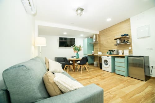 Moderno apartamento de planta abierta en Valencia con sofá gris, mesa de comedor, cocina con lavadora y suelos de madera
