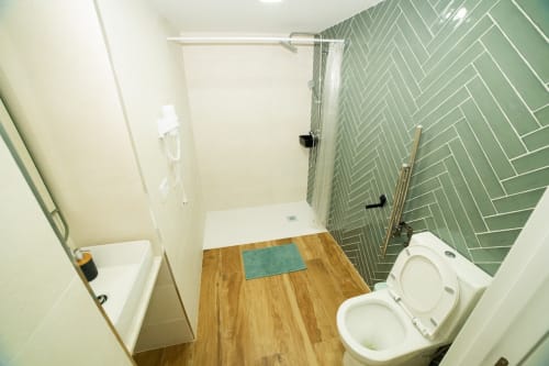 Baño moderno en ML Apartments Valencia con pared de azulejos verdes en espiga, suelo de madera y accesorios blancos