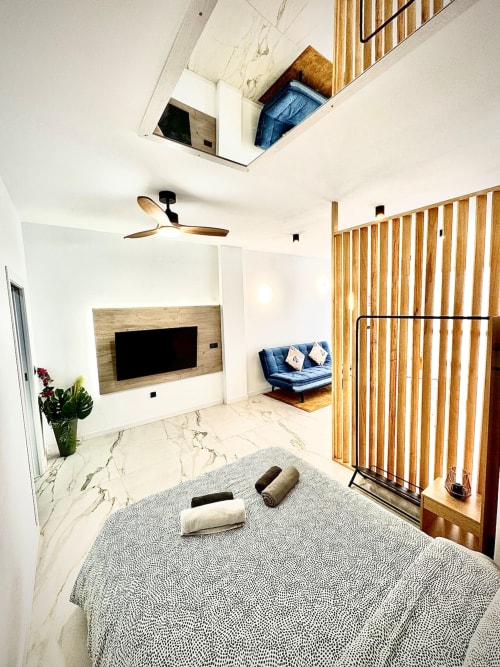 Dormitorio moderno en Valencia con suelos de mármol, pared de listones de madera, ventilador de techo, televisor, futón azul y claraboyas que proporcionan luz natural