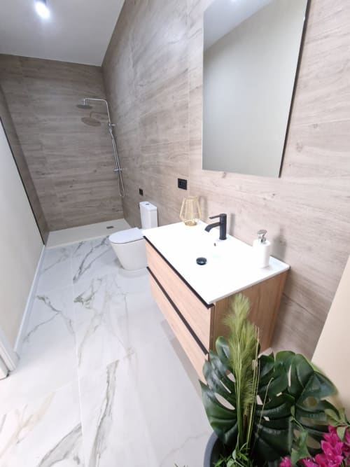 Baño moderno en apartamento de Valencia con suelo de mármol, paredes con azulejos de madera, vanidad blanca, espejo y ducha walk-in