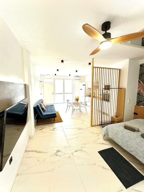 Moderno apartamento de planta abierta en Valencia con ventilador de techo de madera, sofá azul, comedor y piso de mármol