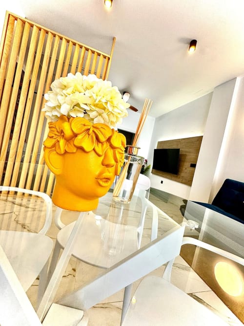 Comedor de apartamento moderno en Valencia con escultura decorativa de cabeza amarilla, flores, sillas blancas y biombo de madera