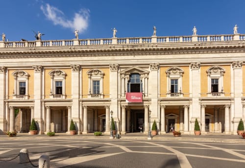 Facciata storica di palazzo romano con colonne gialle e crema, architettura classica e banner rosso del museo