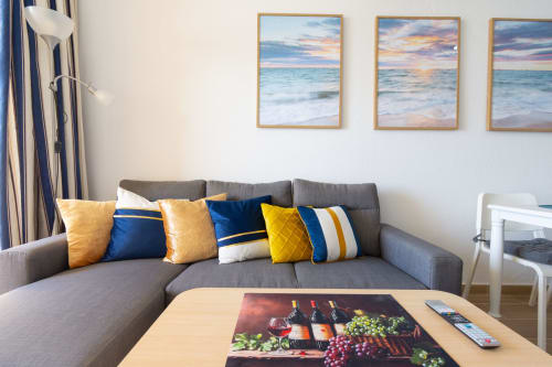Modern living room with gray sofa, colorful pillows, and ocean sunset artwork at Home Stay Gran Canaria