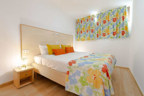 Bright bedroom with white bed, colorful floral bedding, mirrored headboard, and patterned curtains at Home Stay Gran Canaria