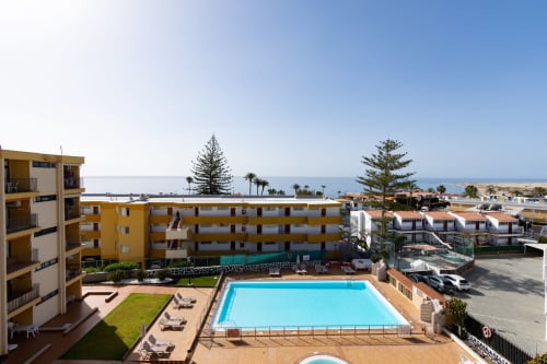 Oceanfront resort in Las Palmas with turquoise pool, yellow apartment buildings, and sea views, Gran Canaria