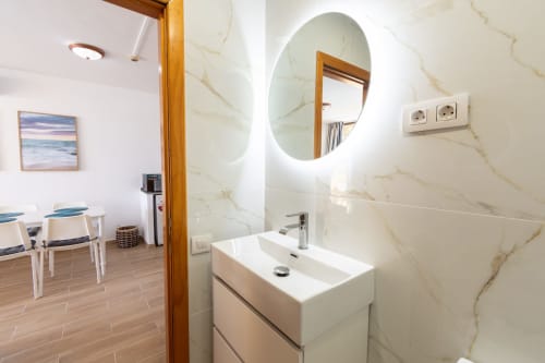 Modern bathroom in Sunset Bay 509 apartment at Home Stay Gran Canaria with marble walls, illuminated mirror, and sink vanity