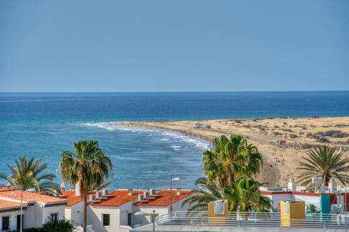 Oceanfront view from Sunset Bay 509 in Gran Canaria with beach, palm trees, and colorful apartments overlooking turquoise