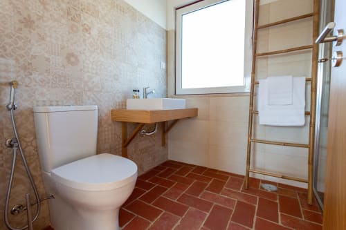 Banheiro moderno da Pousada Cerro da Campaniça em Santiago do Cacém com lavatório de madeira, vaso sanitário branco e piso de terracota