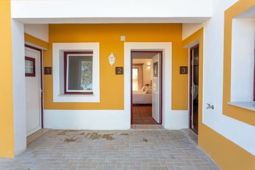 Corredor exterior amarelo brilhante da Pousada Cerro da Campaniça em Santiago do Cacém com portas numeradas e vistas para a serra
