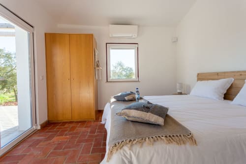 Quarto luminoso da Pousada Cerro da Campaniça em Santiago do Cacém com guarda-roupa em madeira, piso em barro e vista para a serra