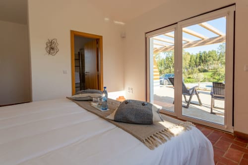 Quarto luminoso em Cerro da Campaniça com cama, vistas de montanha através de portas envidraçadas e acesso ao terraço em Santiago do Cacém