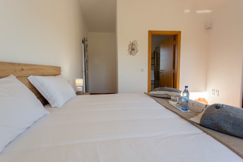 Quarto iluminado na Pousada Cerro da Campaniça em Santiago do Cacém com cama de madeira, roupa de cama branca e vista para as montanhas