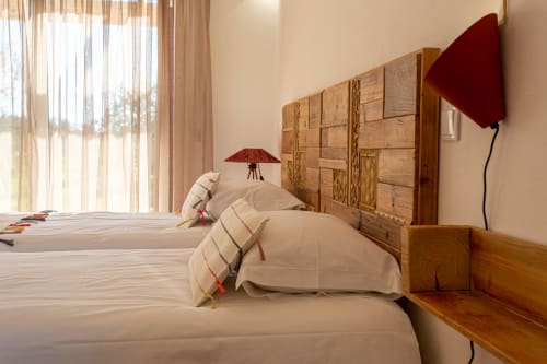 Quarto luminoso em Cerro da Campaniça com cabeceira de madeira, roupa de cama creme, detalhes em vermelho, vista para o jardim e comodidades modernas