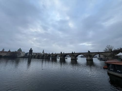Charles Bridge spanning the Vltava River with Prague's Old Town skyline and historic architecture under cloudy skies
