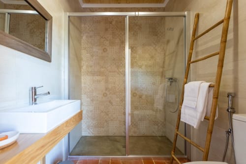 Banheiro moderno com box de vidro, pia branca e escada de toalhas em bambu na Pousada Cerro da Campaniça