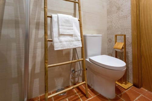 Banheiro moderno na Pousada Cerro da Campaniça com sanitário branco, toalheiro em bambu, azulejos de terracota e box de chuveiro