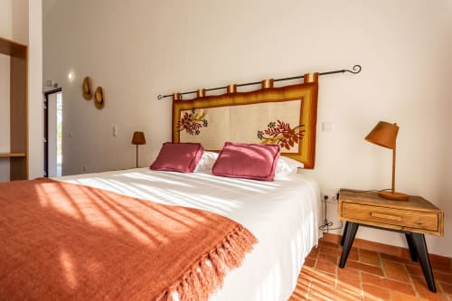 Quarto luminoso em Cerro da Campaniça com cama queen, cabeceira em madeira, almofadas rosa, manta laranja e vista para o jardim