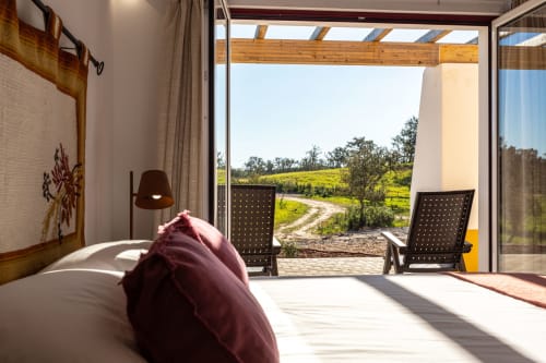 Quarto luminoso em Cerro da Campaniça com almofada bordô, vistas do jardim por portas de vidro abertas, vigas de madeira
