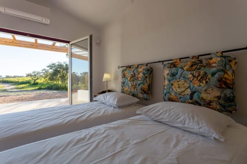 Quarto moderno em Cerro da Campaniça com camas gêmeas, cabeceiras florais e vista do jardim através de janelas piso-teto