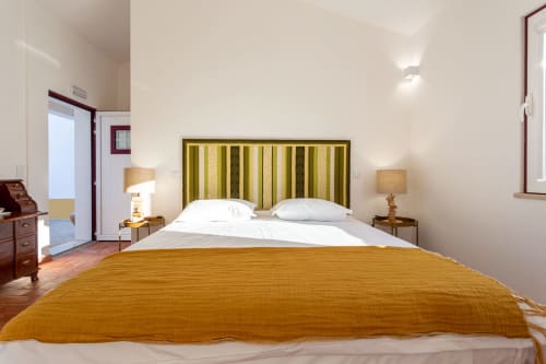 Quarto luminoso na Pousada Cerro da Campaniça com cabeceira listrada, roupa de cama dourada, luminárias geminadas e vista para o jardim em Santiago do
