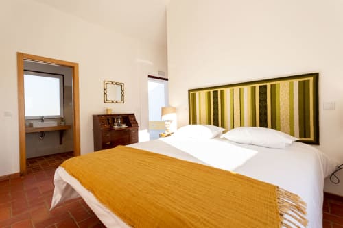 Quarto luminoso na Cerro da Campaniça B&B com cabeceira às riscas, roupa de cama branca e vista para o jardim em Santiago do Cacém